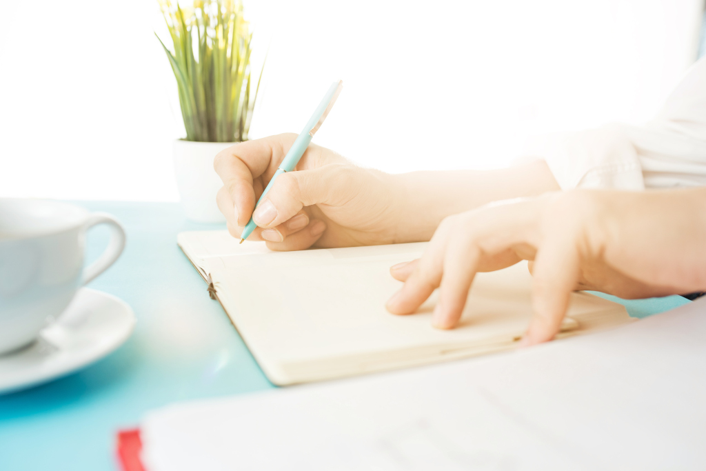 Jemand schreibt mit dem Stift in ein Notizbuch, man sieht nur die Hände auf dem Tisch, Titelbild "Befolge keine Schreibtipps", besser bloggen, regelmäßig schreiben, produktiv bloggen
