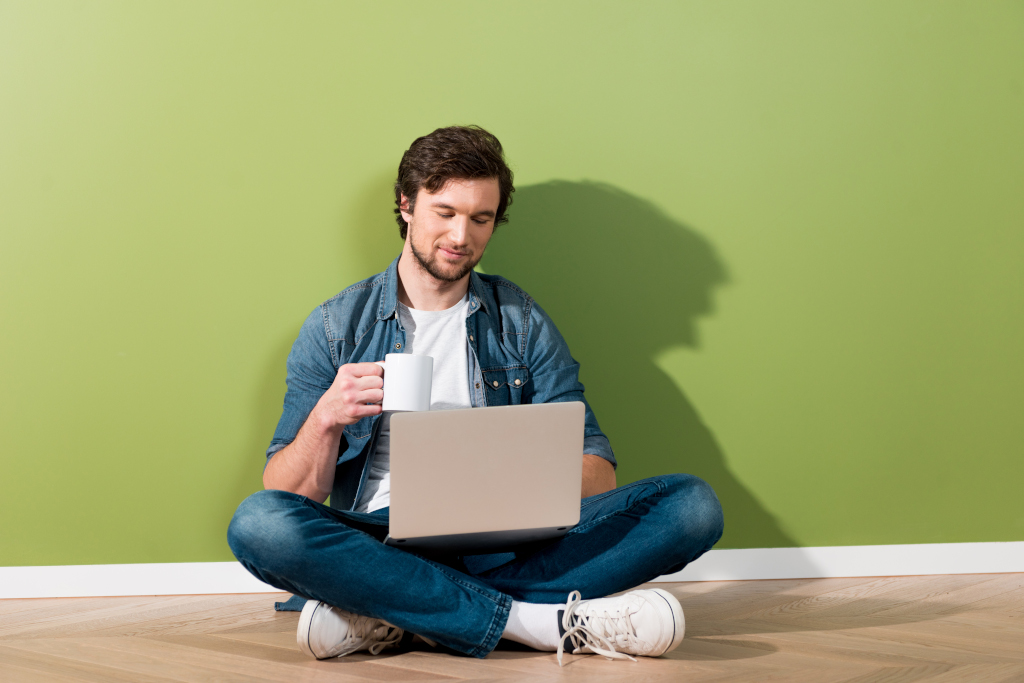 Regelmäßig Content veröffentlichen, entspannt bloggen Symbolbild, Mann sitz entspannt mit Laptop und Kaffeetasse auf dem Boden und arbeitet