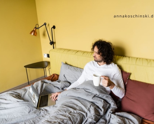 Mann sitzt mit seinem Laptop im Bett und hat eine Kaffeetasse in der Hand, Blognacht, produktiv bloggen, Networking
