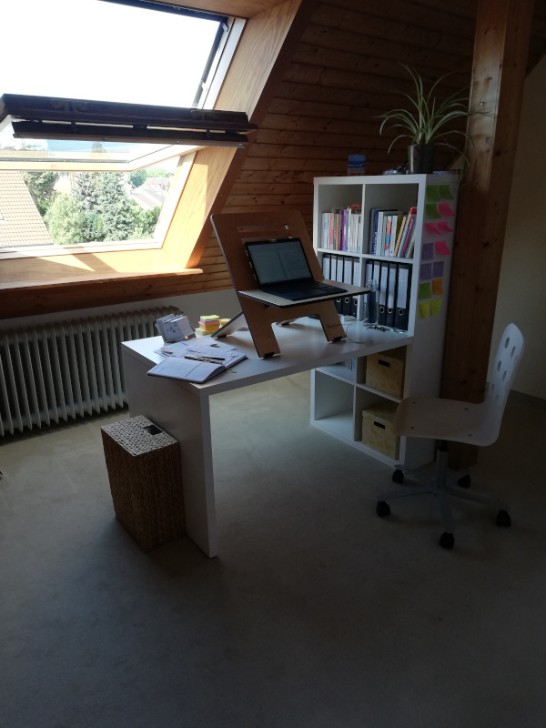 Ein Schreibtisch in einem hellen Dachraum. Auf dem Schreibtisch steht ein Standsome, eine Erhöhung, um im Stehen zu arbeiten.