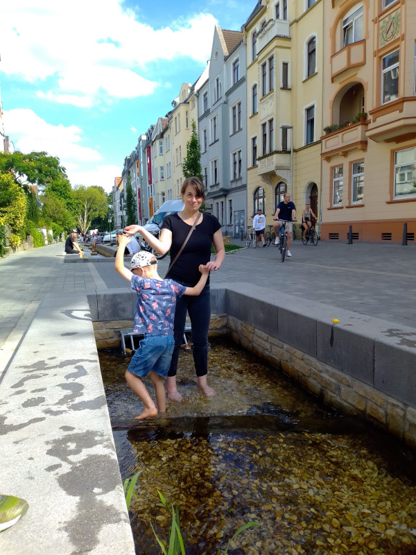 Anna steht mit Junior an der Hand barfuß in der freigelegten Lutter - ein Mini-Flüsschen, das durch Bielefeld fließt.